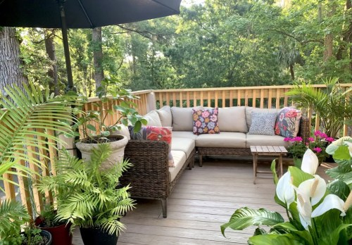 Cozy outdoor seating area with cushions, surrounded by lush greenery and potted plants on a wooden deck.