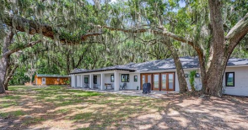 A serene outdoor view of a house surrounded by large trees with Spanish moss, featuring a spacious lawn.