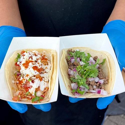 Two tacos in white trays: one with shredded chicken, cheese, and salsa; the other with beef, onions, and cilantro.