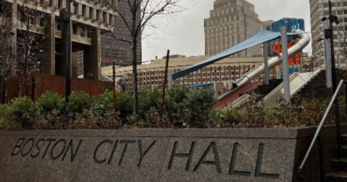 View of Boston City Hall with modern architecture and a colorful slide in the background, surrounded by greenery.