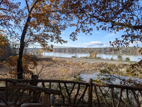 Scenic view of a river with autumn foliage and a bridge in the background under a clear blue sky.