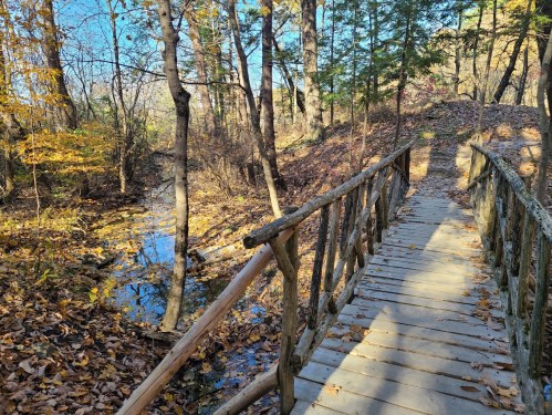 A wooden bridge over a small creek surrounded by trees and autumn foliage.