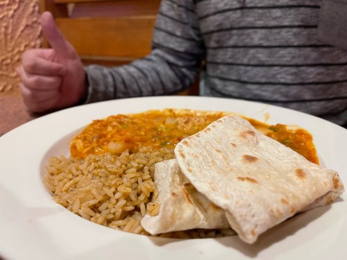 A plate of rice and a savory dish with tortillas, with a person giving a thumbs up in the background.