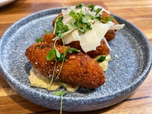 A plate of golden-brown croquettes topped with herbs and cheese, served on a creamy sauce.