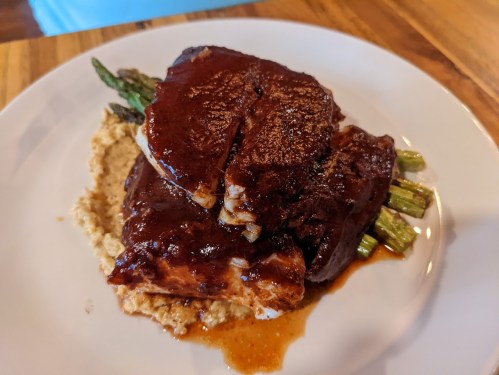 A plate featuring sliced meat with a rich sauce, served on a bed of creamy puree and topped with asparagus.