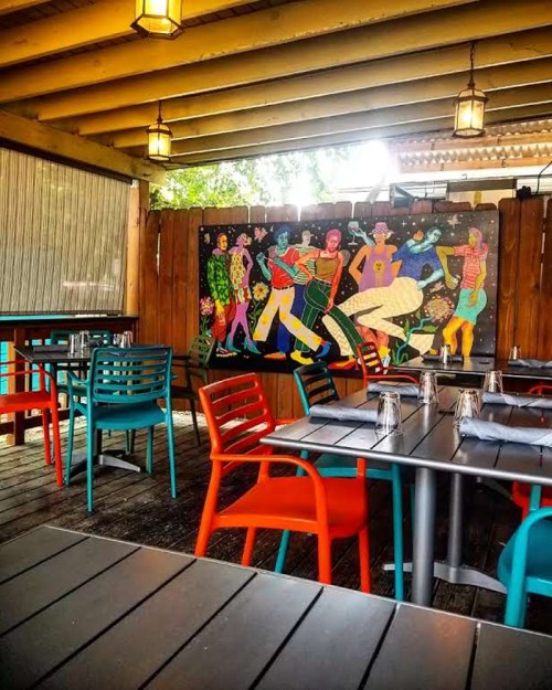 Colorful outdoor dining area with vibrant chairs and a lively mural depicting dancing figures on the wall.