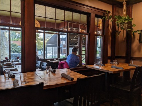 A cozy restaurant interior with wooden tables, empty glasses, and a person sitting by the window, looking outside.