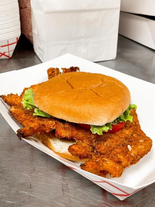 A crispy fried chicken sandwich with lettuce and tomato on a soft bun, served in a white tray.