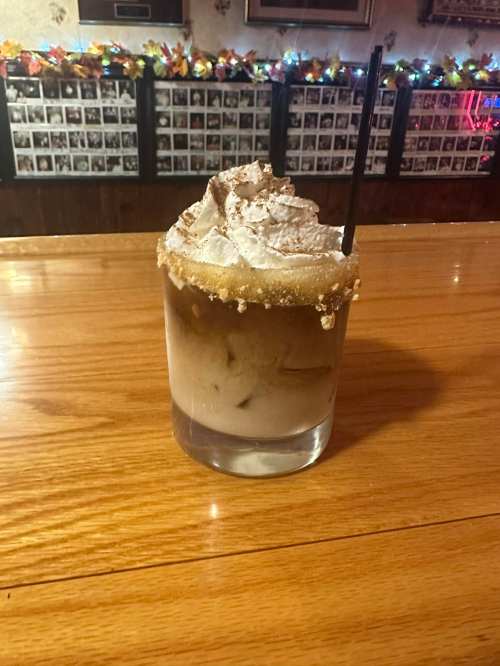 A glass of iced drink topped with whipped cream and a sugared rim, sitting on a wooden bar counter.