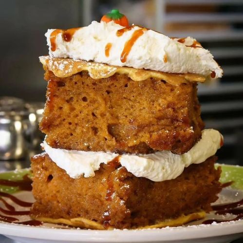 A close-up of two layers of moist cake topped with whipped cream and drizzled with caramel sauce on a plate.