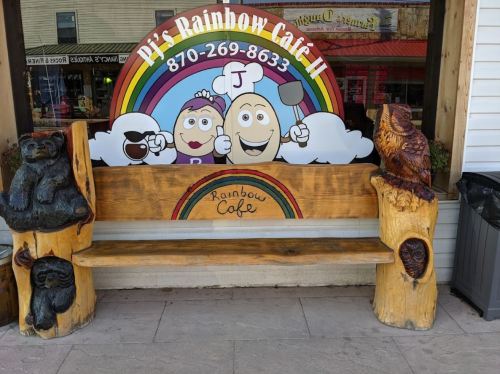 A wooden bench with carved animal figures, in front of a colorful café sign featuring cartoon characters and a rainbow.