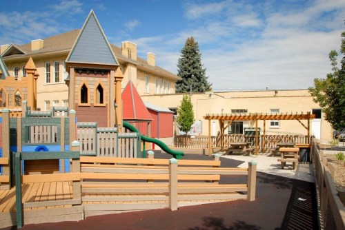 Colorful playground with slides and climbing structures, surrounded by trees and a picnic area under a blue sky.