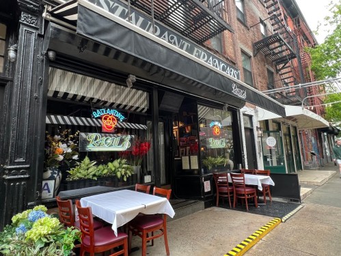 Exterior of a restaurant with a striped awning, outdoor seating, and large windows displaying floral arrangements.
