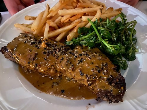 A plate featuring a seasoned steak with sauce, served alongside fries and sautéed greens.