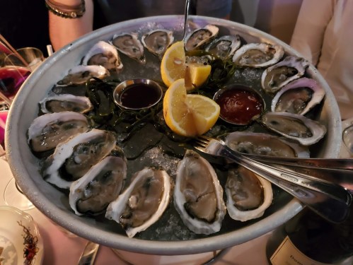 A platter of fresh oysters on ice, garnished with lemon wedges and served with dipping sauces.
