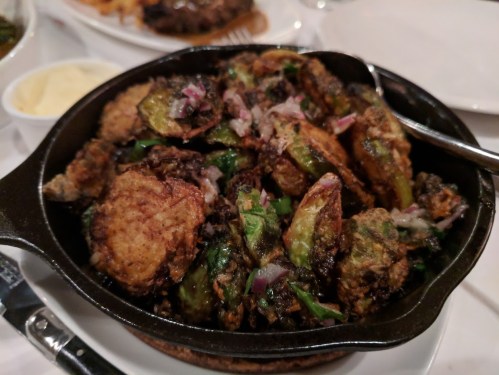 A sizzling cast-iron dish filled with crispy fried vegetables, garnished with herbs and onions.