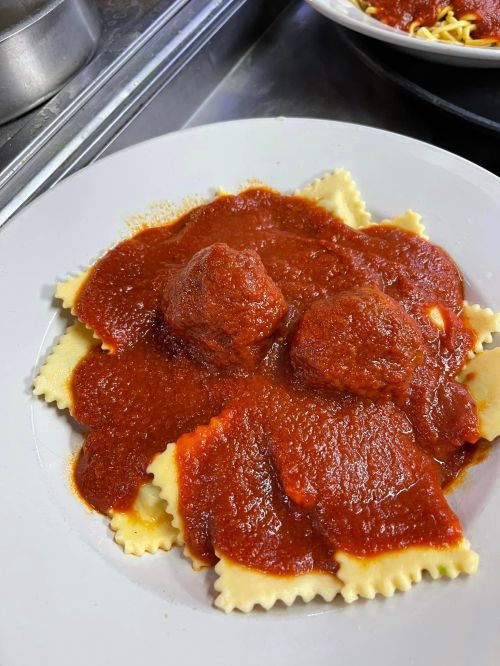A plate of ravioli topped with marinara sauce and meatballs, served on a white dish.