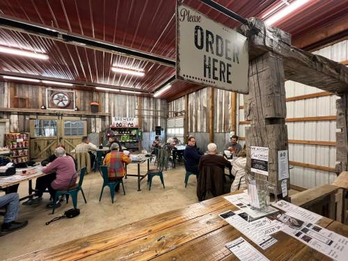 A rustic dining area with patrons seated at tables, a sign reading "Please Order Here," and wooden decor.