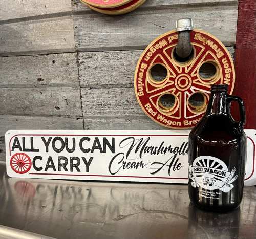 A sign reading "All You Can Carry" next to a growler of Marshmallow Cream Ale and a decorative red wagon wheel.
