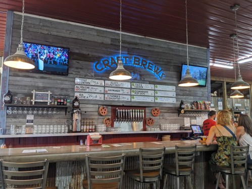A rustic bar with a wooden wall, craft beer taps, and patrons enjoying drinks in a lively atmosphere.