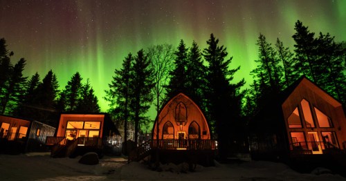 Four unique cabins in Alaska against the tree line with the Northern Lights.