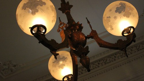 A vintage chandelier with three glowing globes, featuring ornate detailing and floral designs.