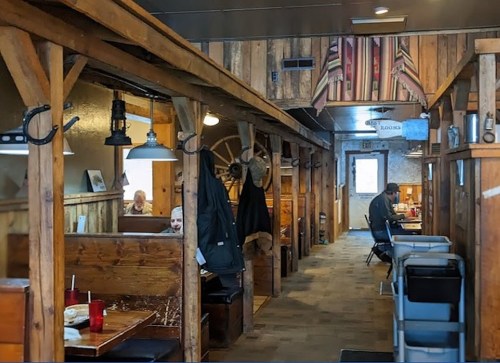A cozy wooden restaurant interior with booths, hanging coats, and a few diners enjoying their meals.