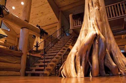 A spacious log cabin interior featuring a large tree trunk and a wooden staircase leading to an upper level.