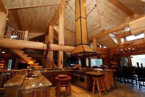 A spacious rustic kitchen with wooden beams, a large island, and a unique hood over the stove, featuring natural decor.