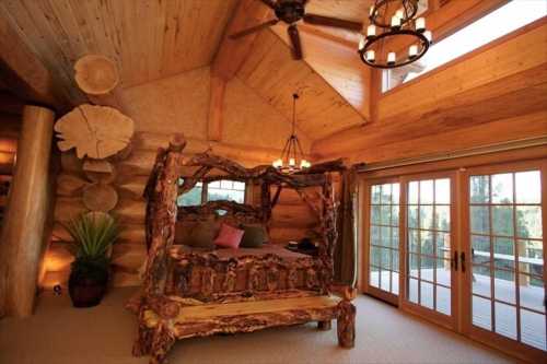 Cozy log cabin bedroom featuring a rustic wooden bed, large windows, and natural decor elements.