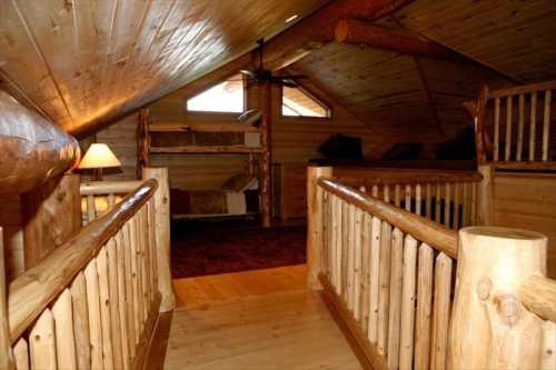 Cozy wooden loft with a sloped ceiling, featuring a railing, bunk beds, and warm lighting.