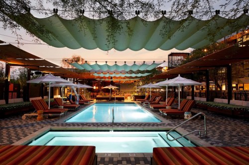 A serene pool area with lounge chairs and umbrellas, surrounded by shaded canopies at dusk.