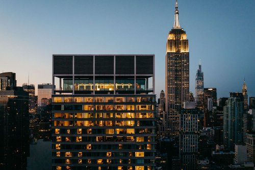 A city skyline at dusk featuring the Empire State Building and a modern building with illuminated windows.