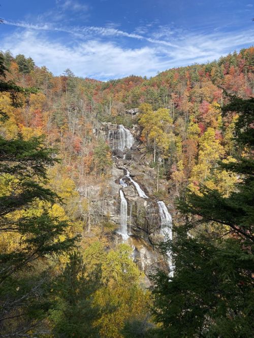 A scenic waterfall surrounded by vibrant autumn foliage and blue skies.