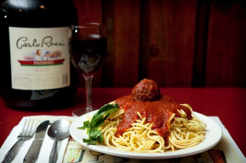 A plate of spaghetti topped with marinara sauce and a meatball, accompanied by a glass of red wine and a large wine bottle.