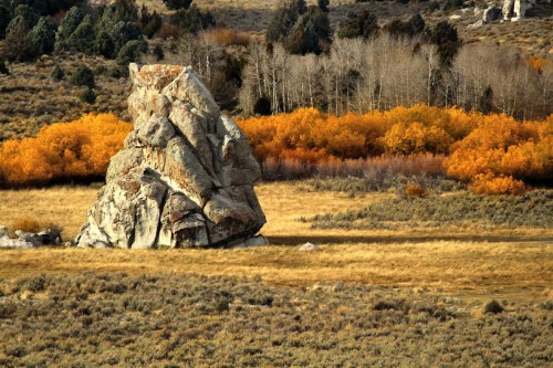 A large rock stands in a grassy field, surrounded by autumn trees with vibrant orange leaves.