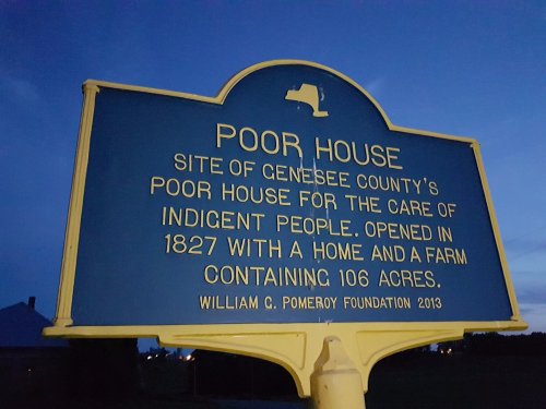 Sign reading "Poor House" detailing the history of Genesee County's care facility for the indigent, established in 1827.