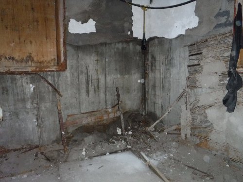 A dilapidated room with cracked walls, exposed concrete, and debris scattered on the floor.