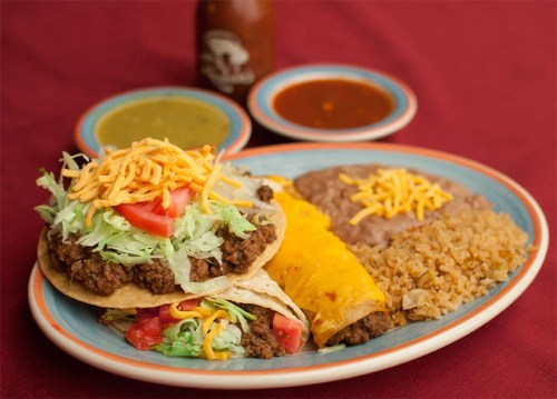 A colorful plate featuring tacos, rice, refried beans, and sauces, garnished with lettuce, tomato, and cheese.