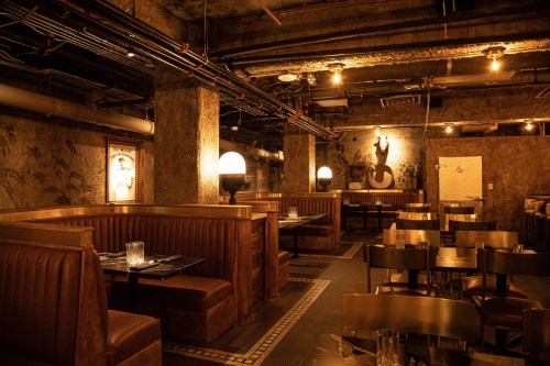 Dimly lit restaurant interior with leather booths, wooden tables, and industrial decor. Warm ambiance with soft lighting.