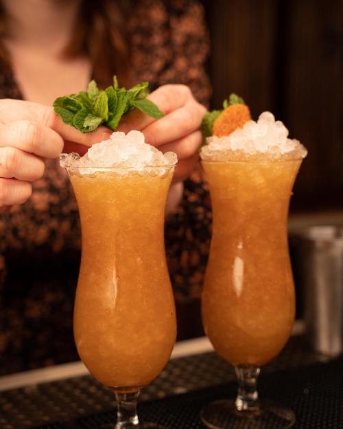 Two tall glasses filled with a frosty cocktail, topped with crushed ice and garnished with mint leaves.