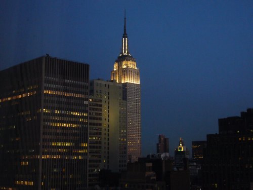 The Empire State Building illuminated at night, surrounded by city skyscrapers under a dark blue sky.