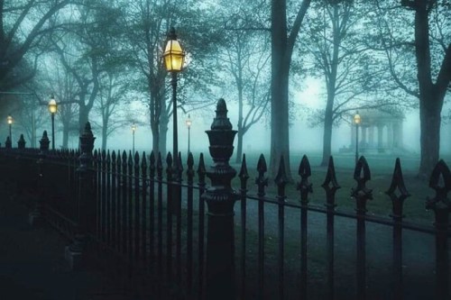 A misty park scene with a wrought iron fence and glowing street lamps illuminating the foggy atmosphere.