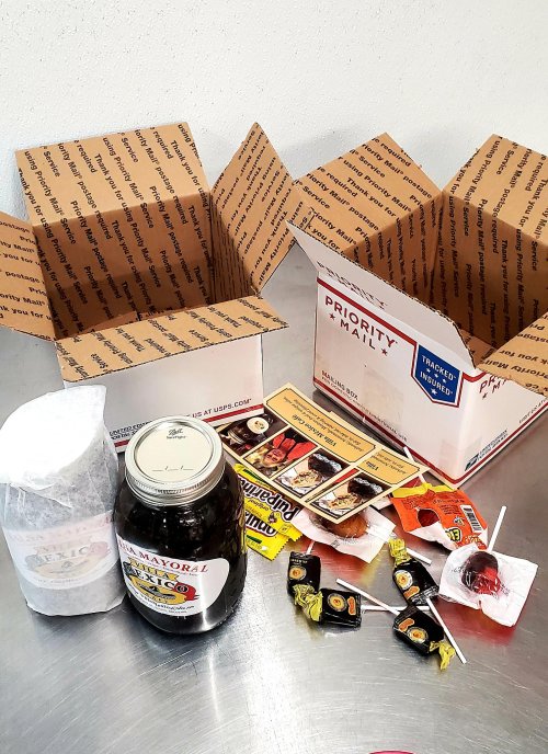 Two empty priority mail boxes next to various snacks, including candies, a jar of salsa, and a wrapped item.