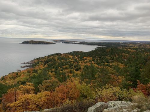 A scenic view of a coastline with colorful autumn foliage and a cloudy sky over the water.