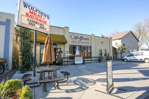 Exterior of Wolfsen's Meat & Sausage shop, featuring a sign, outdoor seating, and a clear blue sky.