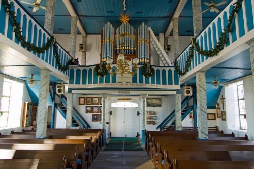 Interior of a church featuring blue accents, wooden pews, an organ, and festive decorations.