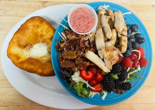A colorful plate with grilled chicken, mixed berries, salad, and a fried bread on the side, served with a dipping sauce.