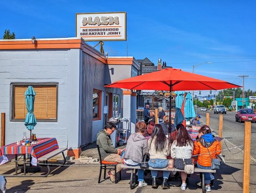A group of people dining at an outdoor table under a red umbrella outside a breakfast restaurant.