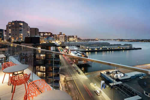 City skyline at dusk with waterfront views, modern buildings, and illuminated streets from a balcony perspective.